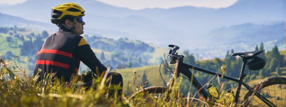sportgardena-man-cyclist-sitting-grass-looking-mountains